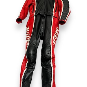 May include: Black and red motorcycle racing suit with white accents. The suit is made of leather and features a full-length zipper, knee pads, and the brand name "Dainese" printed on the legs. The suit is hanging on a hanger.