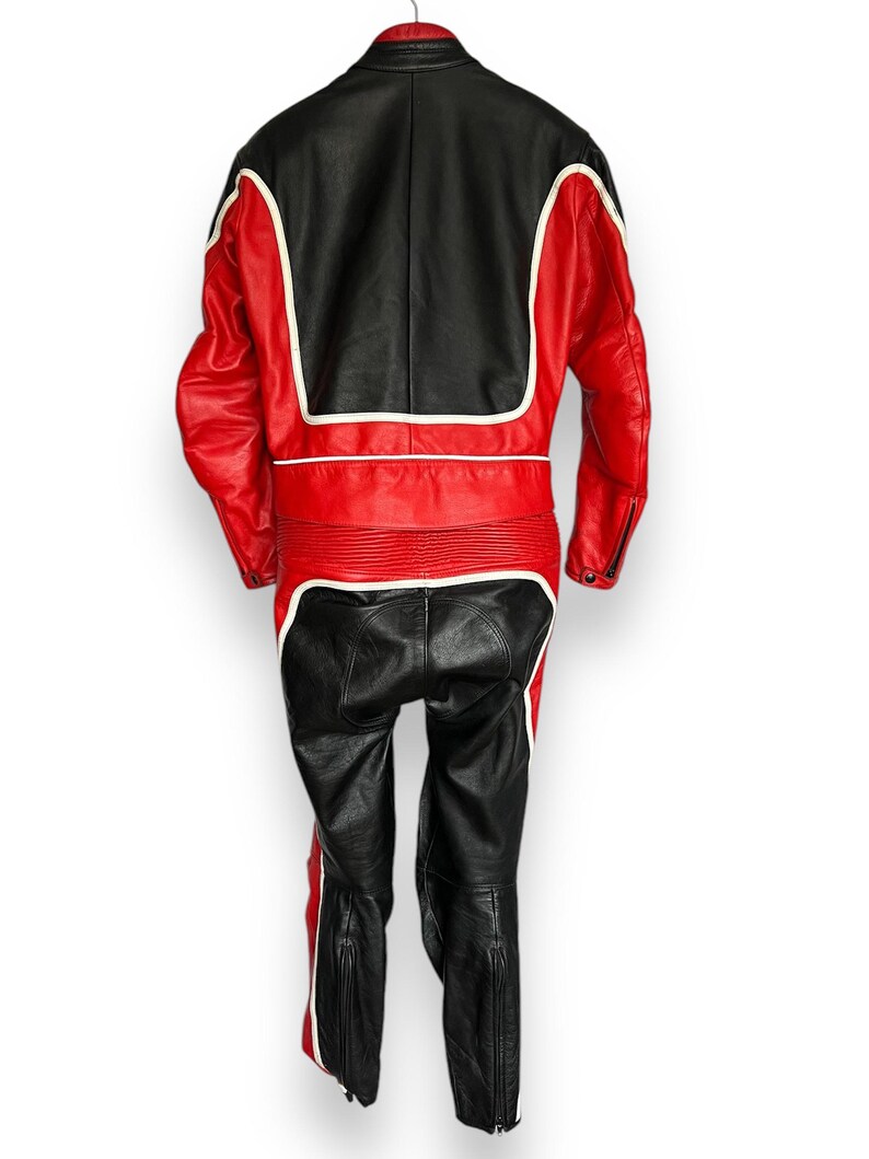 May include: A two-piece motorcycle suit in black and red leather with white accents. The jacket features a black upper back and red sleeves and torso. The pants are black with red and white stripes down the sides. The suit has zippers on the sleeves and legs.