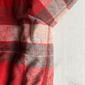 Op de afbeelding: Close-up van een rood, bruin en beige geruit flanellen overhemd. De stof heeft een zachte textuur en een klassiek patroon. De mouw en een deel van de body van het overhemd zijn zichtbaar, wat het traditionele ontwerp laat zien.