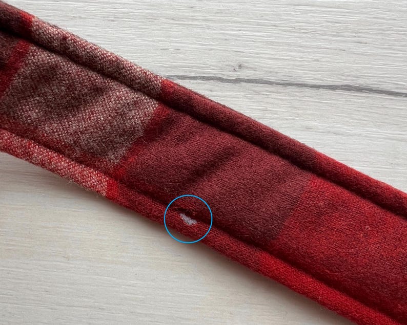 Op de afbeelding: Close-up van een rood en bordeaux geruite hoofdband. De hoofdband is gemaakt van een zachte, getextureerde stof. Het ruitpatroon heeft een mix van rode en bordeaux tinten, wat een warme uitstraling cre&euml;ert. De hoofdband is ontworpen om om het hoofd te worden gedragen.