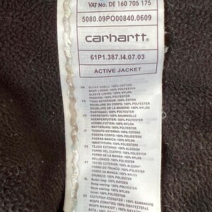 May include: A close-up of a Carhartt Active Jacket label. The label is white with black text, including the brand name and fabric composition details. The jacket's outer shell is 100% cotton, with a polyester body lining and nylon sleeve lining.