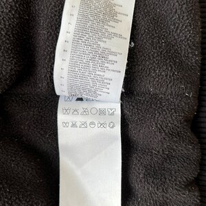 May include: Close-up of a black garment with a white tag attached. The tag contains text in multiple languages detailing fabric composition and care instructions. The bottom of the tag reads "MADE IN CHINA".