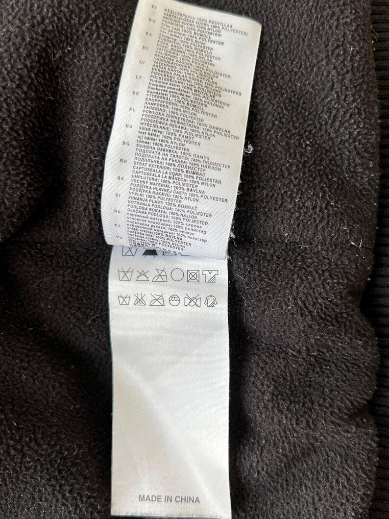 May include: Close-up of a black garment with a white tag attached. The tag contains text in multiple languages detailing fabric composition and care instructions. The bottom of the tag reads "MADE IN CHINA".