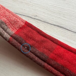 Op de afbeelding: Close-up van een rood en bruin geruit weefsel. De stof heeft een gestikt ontwerp en is gemaakt van een zacht materiaal. Het ruitpatroon heeft vierkanten in rood, bruin en beige.