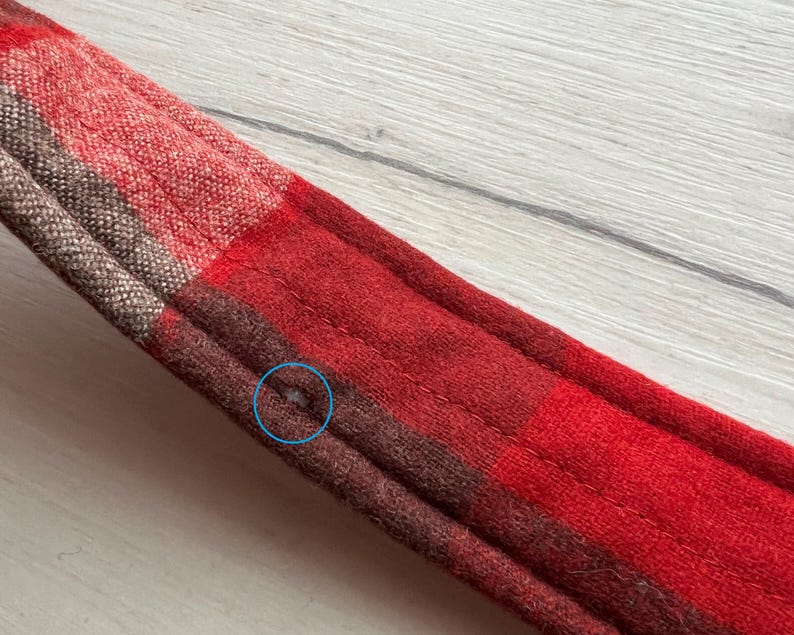 Op de afbeelding: Close-up van een rood en bruin geruit weefsel. De stof heeft een gestikt ontwerp en is gemaakt van een zacht materiaal. Het ruitpatroon heeft vierkanten in rood, bruin en beige.