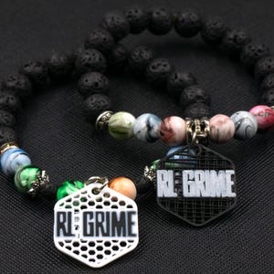 May include: Two beaded bracelets. One bracelet features black lava beads and colorful accent beads. Each bracelet has a hexagonal charm with the text "RE GRIME". One charm is white, the other is black.
