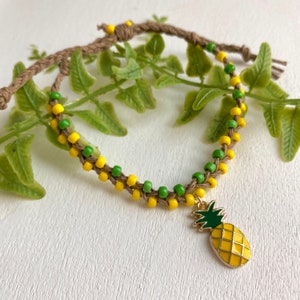 May include: A yellow and green beaded bracelet with a pineapple charm. The bracelet is made of brown string and is tied with a knot.