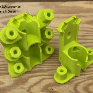 May include: Two bright green scrubber holders with multiple circular openings and a curved design. The text "Scrubber & Accessories Holders in Green" is at the top left. The holders are on a wooden surface.