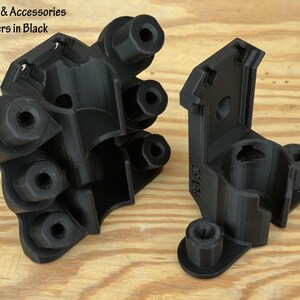 May include: Two black plastic scrubber and accessory holders. The holders are 3D-printed and have a geometric design with multiple circular openings and mounting points. The text "Scrubber & Accessories Holders in Black" is visible.