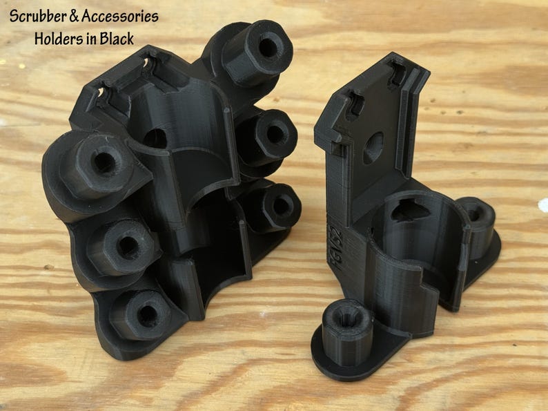 May include: Two black plastic scrubber and accessory holders. The holders are 3D-printed and have a geometric design with multiple circular openings and mounting points. The text "Scrubber & Accessories Holders in Black" is visible.