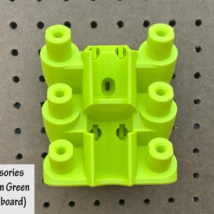 May include: A bright green accessory holder, designed for use with a pegboard. The holder features a rectangular base with several cylindrical posts and a central compartment. The text "Accessories Holder in Green (on pegboard)" is visible.