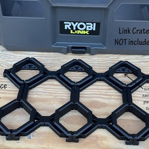 May include: A set of six black plastic hexagonal tiles with screw holes on each end for attaching to a surface. The tiles are arranged in a honeycomb pattern. The text "6-piece set" is visible in the image. The text "RYOBI LINK" and "Link Crate NOT included" is visible on a gray toolbox in the background.