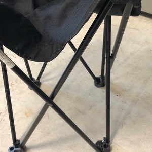 May include: Black folding chair with a metal frame and black fabric seat. The chair is folded and the legs are visible.