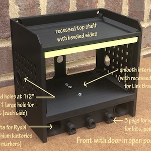 May include: Black 3D printed storage organizer with a door, two shelves, and pegboard holes. The top shelf has beveled sides and the bottom shelf has recessed screws. The organizer has slots for batteries and pegs for holding small items.