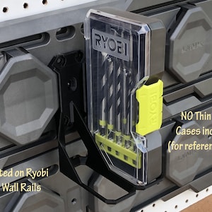 May include: A black metal wall mount for holding Ryobi drill bit cases. The mount is attached to a gray Ryobi Link Wall Rail system. The image shows a clear plastic case with Ryobi drill bits inside. The text "NO Thin Bits Cases included (for reference only)" is visible in the image.