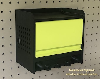 Puede incluir: Unidad de almacenamiento de tablero de clavijas negro con una puerta de color amarillo brillante. La puerta está cerrada y la unidad está montada en una pared de tablero de clavijas.