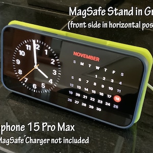 May include: A green and blue MagSafe stand displaying a clock and calendar. The screen shows the date, November 18th, and the time. The stand is designed for an iPhone 15 Pro Max.