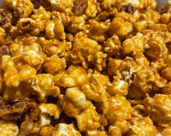 May include: A close-up of a bowl filled with caramel popcorn and pecans. The popcorn is golden brown and the pecans are scattered throughout.
