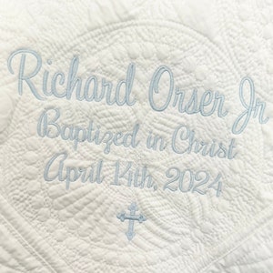 May include: White quilted baby blanket with blue embroidery that reads "Richard Orser Jr. Baptized in Christ April 14th, 2024".