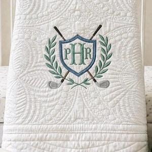 May include: A white baby crib with a golf theme. The crib has a white quilt with a golf emblem, a golf bag that says "Baby Golfer", a golf cart, golf balls, and a book titled "My First Golf Book".