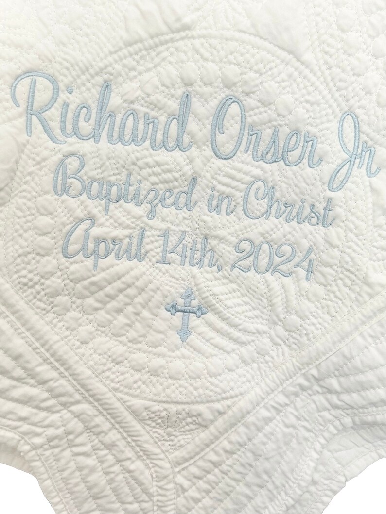 May include: White quilted baby blanket with blue embroidery that reads "Richard Orser Jr. Baptized in Christ April 14th, 2024".
