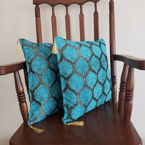 May include: Two turquoise blue throw pillows with gold tassels and a geometric pattern on a wooden chair.