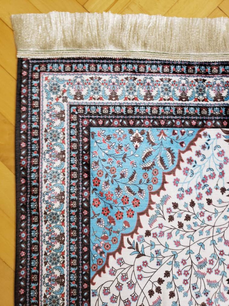 Op de afbeelding: Een blauw en wit gebedskleed met een bloemenpatroon en een franje rand. Het kleed heeft een traditioneel ontwerp met ingewikkelde details.