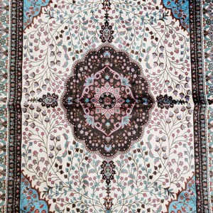Op de afbeelding: Een wit tapijt met een bruin en blauw bloemenpatroon. Het tapijt heeft een centraal medaillon met een geometrisch ontwerp.