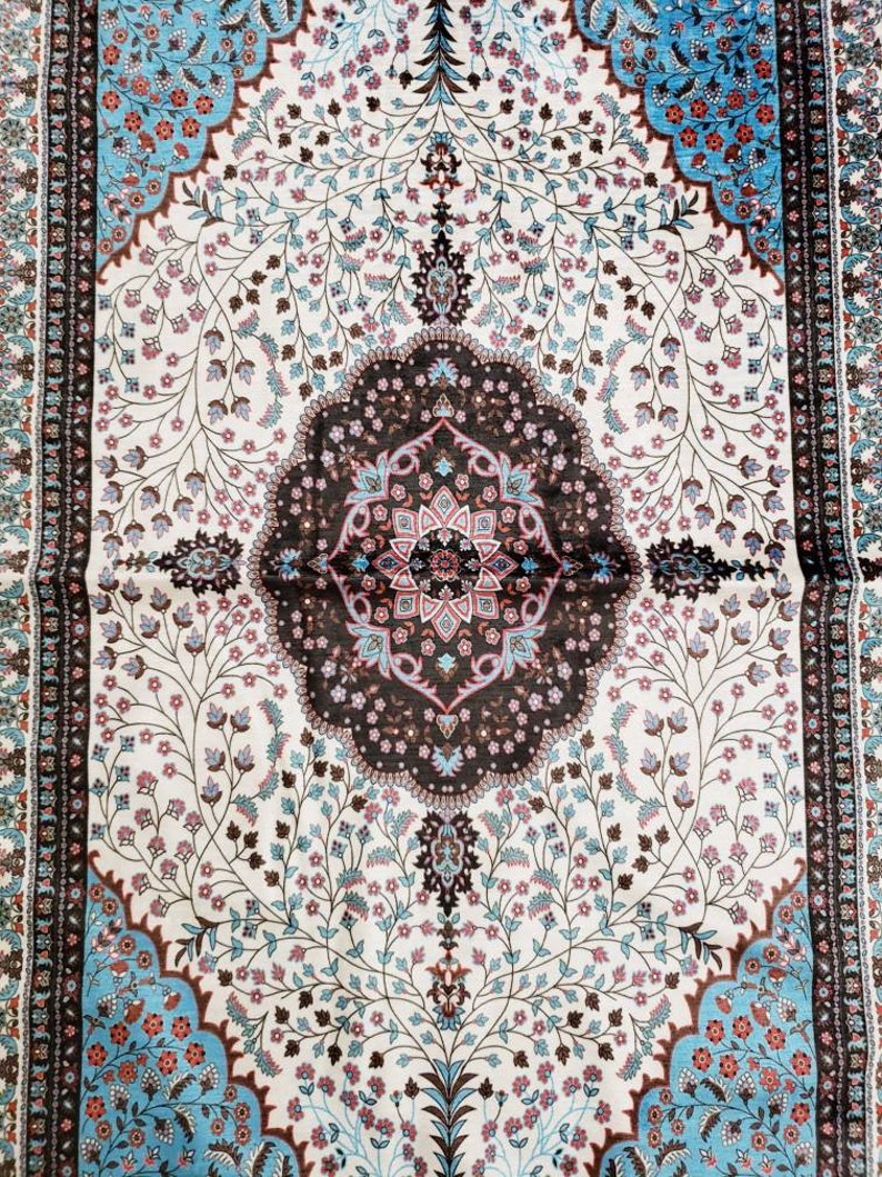 Op de afbeelding: Een wit tapijt met een bruin en blauw bloemenpatroon. Het tapijt heeft een centraal medaillon met een geometrisch ontwerp.