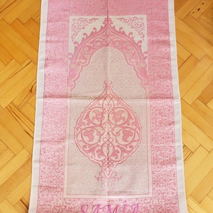 May include: A pink and white prayer rug with a floral design and the name "SAMIA" embroidered in pink.