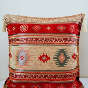 Puede incluir: Una almohada de tiro roja, beige y verde con borlas. La almohada tiene un diseño geométrico con un motivo central en forma de diamante.