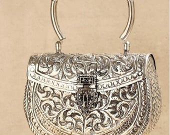 May include: A silver handbag with an ornate floral design and a top handle. The bag has a hinged clasp.