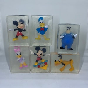 May include: Six clear plastic cubes with different Disney characters inside. Mickey Mouse is shown in two poses, one on a skateboard and the other with his arms outstretched. Donald Duck is shown with his arms outstretched. Minnie Mouse is shown with her arms at her sides. Goofy is shown with his arms at his sides. Pluto is shown with his tongue sticking out.