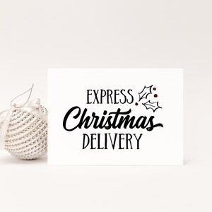 May include: A white Christmas card with the words "EXPRESS Christmas DELIVERY" in black script and a sprig of holly with red berries. A silver bauble with a ribbon is to the left.