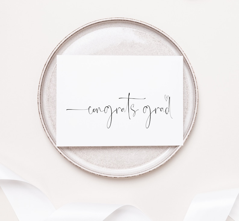 May include: A white card with black calligraphy that reads "congrats grad" with a small heart symbol.