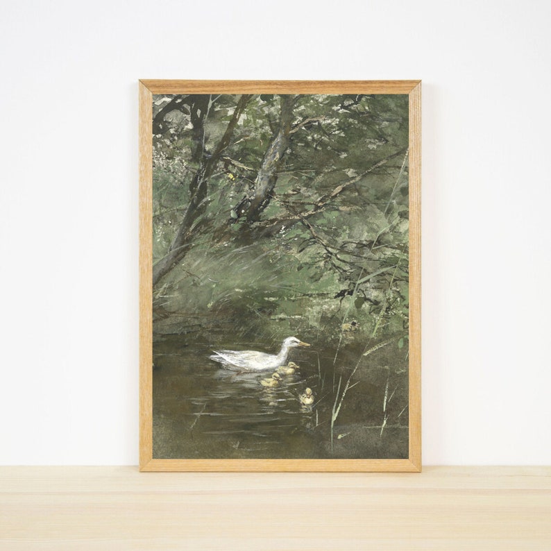 Op de afbeelding: Een ingelijst aquarel schilderij van een witte eend met eendjes die zwemmen in een vijver omringd door groene bomen en bladeren.