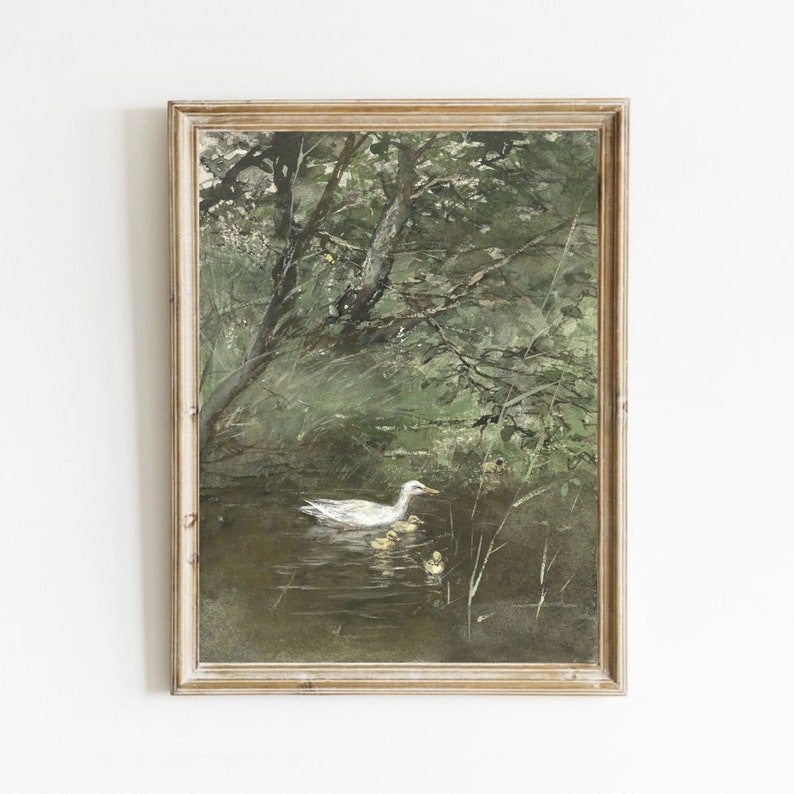 Op de afbeelding: Een ingelijst aquarel schilderij van een witte eend met eendjes die zwemmen in een vijver omringd door groene bomen en bladeren.