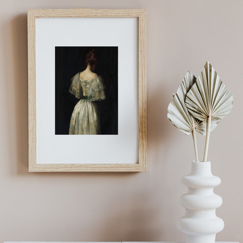 May include: A framed painting of a woman in a white dress with a green sash, standing with her back to the viewer. The painting is set against a dark background.