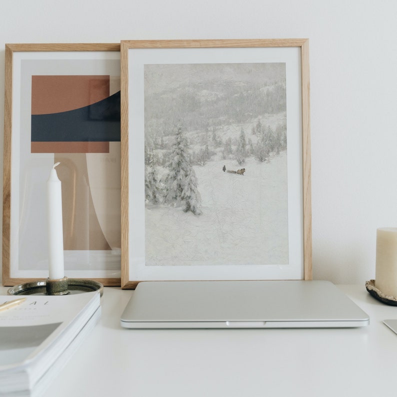 Peut inclure: Deux images encadr&eacute;es sur une surface blanche. L'image de gauche est un design abstrait g&eacute;om&eacute;trique avec des couleurs brunes, beiges et bleues. L'image de droite est un paysage enneig&eacute; avec un petit groupe de personnes et un tra&icirc;neau tir&eacute; par un cheval au loin.