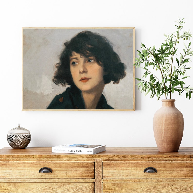 Op de afbeelding: Een ingelijst schilderij van een vrouw met donker haar en een zwarte sjaal. De vrouw kijkt naar links van het frame. De achtergrond is lichtgrijs.