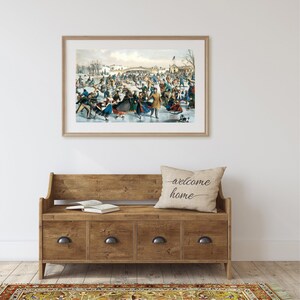 May include: A framed vintage illustration of a winter scene with people ice skating on a frozen lake. The illustration is in a light wood frame and is hanging on a white wall.