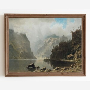 Könnte beinhalten: Ein gerahmtes Ölgemälde, das eine Bergseenlandschaft darstellt. Das Gemälde zeigt eine Wasserfläche, die von Bergen umgeben ist, mit einem dunklen Vogel, der über dem Wasser fliegt. Der Himmel ist bewölkt und das Wasser ist ruhig.