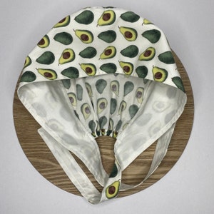 May include: White fabric chef hat with a tie, featuring a repeating pattern of green avocados on a white background.