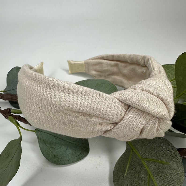 May include: A beige knotted headband made of linen fabric. The headband is a simple, elegant design that can be worn with a variety of outfits.