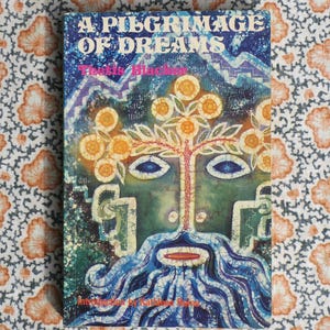 K&ouml;nnte beinhalten: Ein Vintage-Buch mit dem Titel "A Pilgrimage of Dreams" mit einem farbenfrohen, abstrakten Cover-Design. Das Cover zeigt ein gesichts&auml;hnliches Bild mit einem Baum und floralen Elementen in Blau-, Gr&uuml;n- und Gelbt&ouml;nen. Das Buch liegt auf einem gemusterten Stoff.