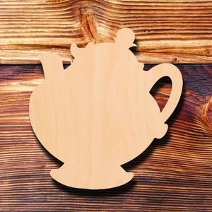 May include: A wooden cutout of a teapot with a handle and spout. The cutout is unpainted and has a smooth, natural wood finish.