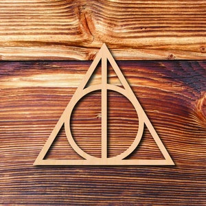 May include: A wooden cutout of the Deathly Hallows symbol, a triangle with a circle inside and a vertical line through the circle, on a brown wood background.