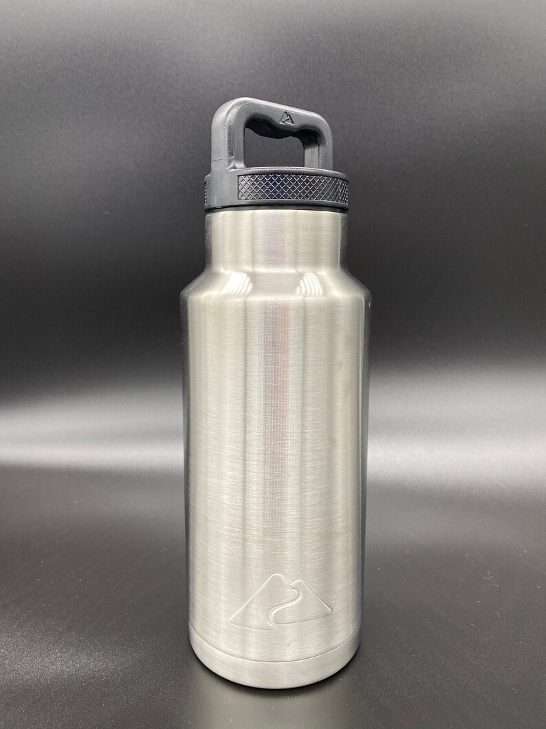 May include: A silver stainless steel water bottle with a black handle and a mountain logo. The bottle has a brushed finish.