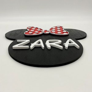 May include: Black wooden sign shaped like Mickey Mouse ears with a red bow with white polka dots and the name "ZARA" in white raised letters.