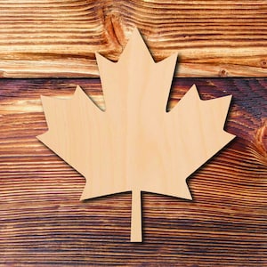 May include: A wooden maple leaf cutout, painted in a light brown color, is placed on a brown wooden surface.